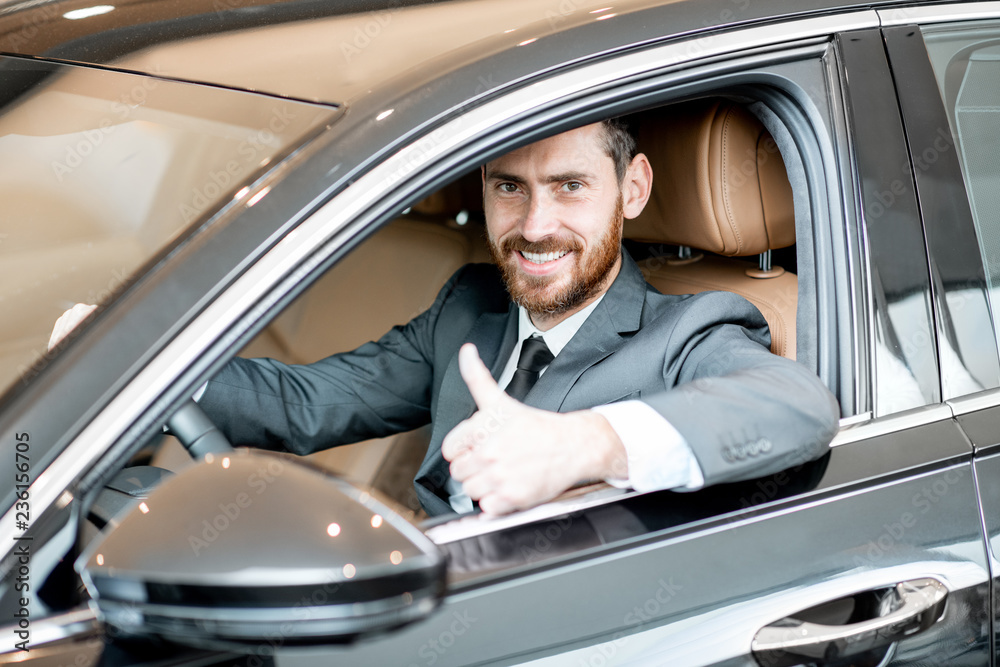 Portrait of an elegant businessman sitting on the driver seat in the luxury car at the showroom