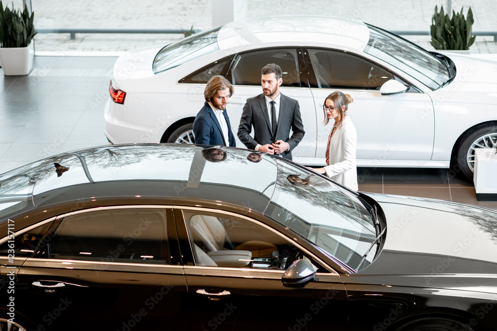 Business couple chosing a new car standing with salesperson in the car showroom. View from above