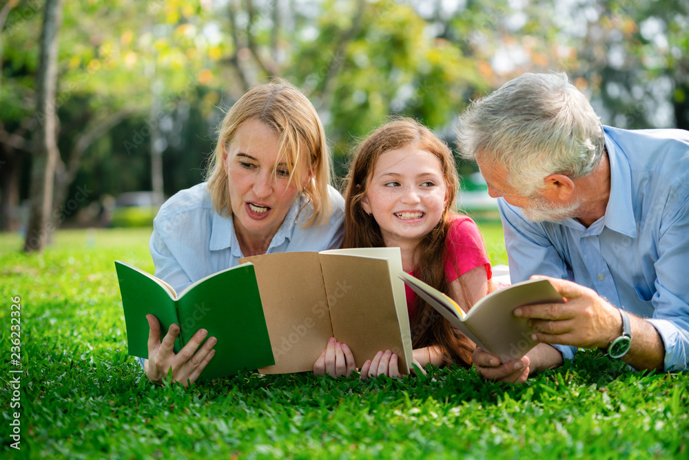 Happy family read books together and lying on green grass in public park. Little girl kid learning w