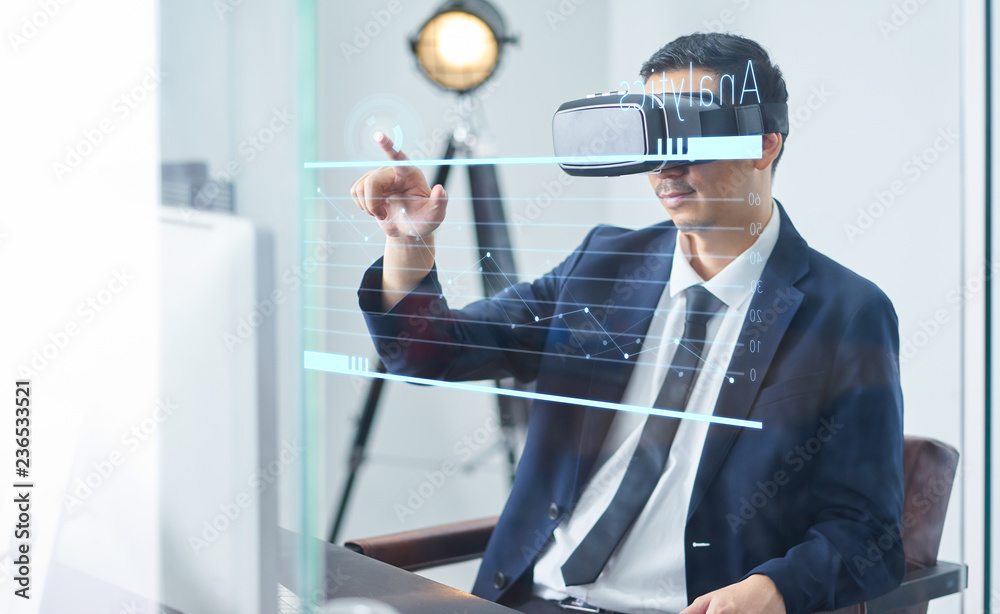 Asian businessman wearing virtual reality goggle and pointing business growth chart in a office .