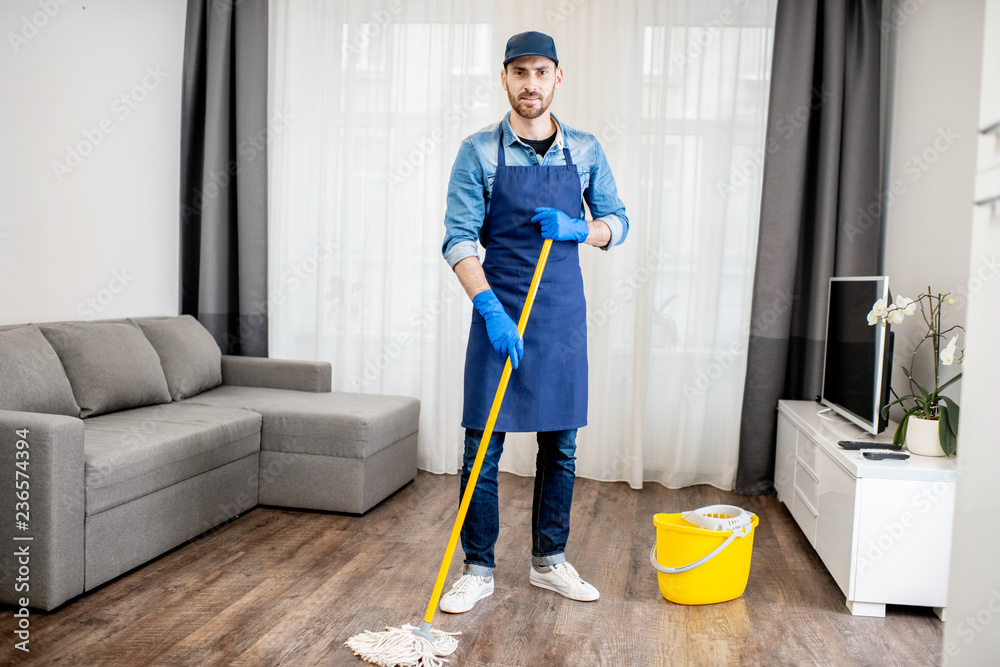 Portrait of a man as a professional cleaner in blue uniform washing floor with mopping stick and buc