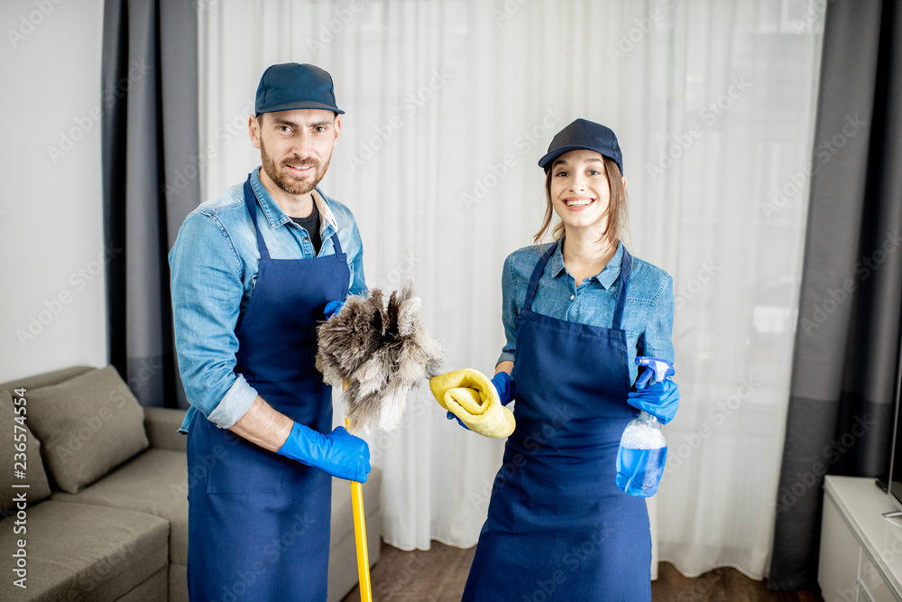 Portrait of a young couple as a professional cleaners in blue uniform with cleaning tools in the apa