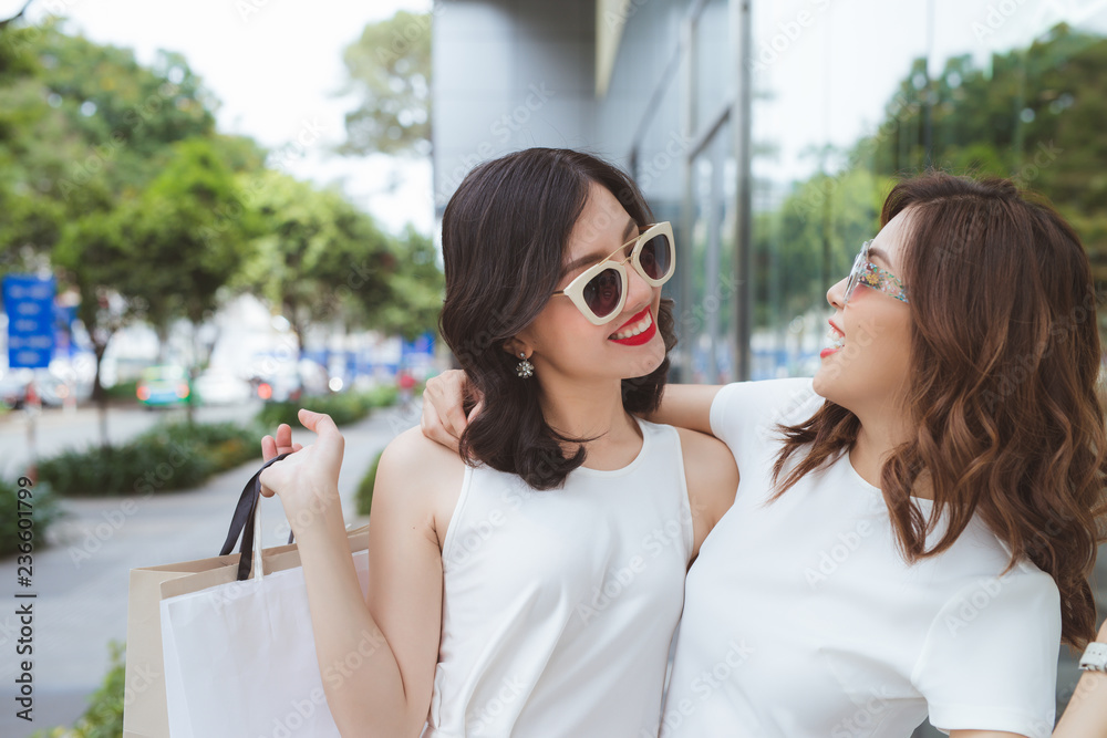 sale, consumerism and people concept - happy young women with shopping bags on city street