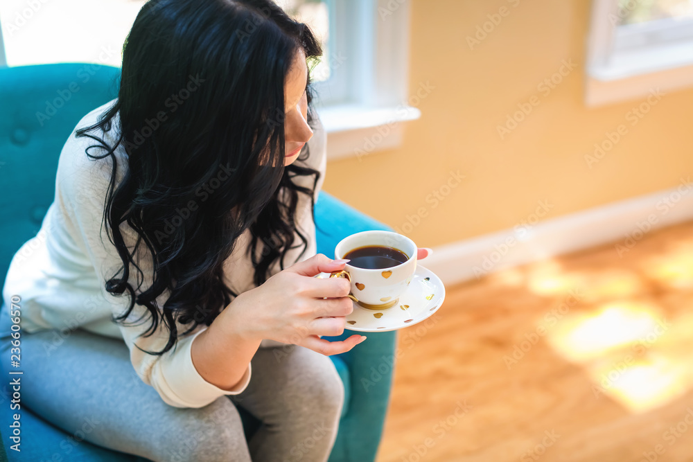 年轻女子在家里的椅子上喝咖啡