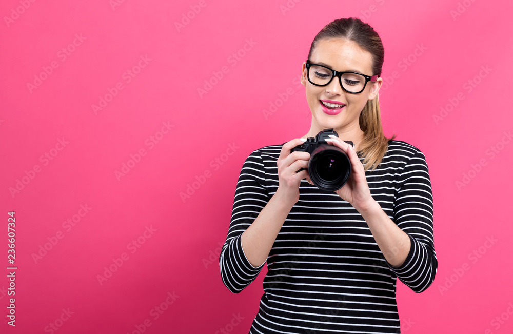 Young woman with a professional digital SLR camera on a pink background