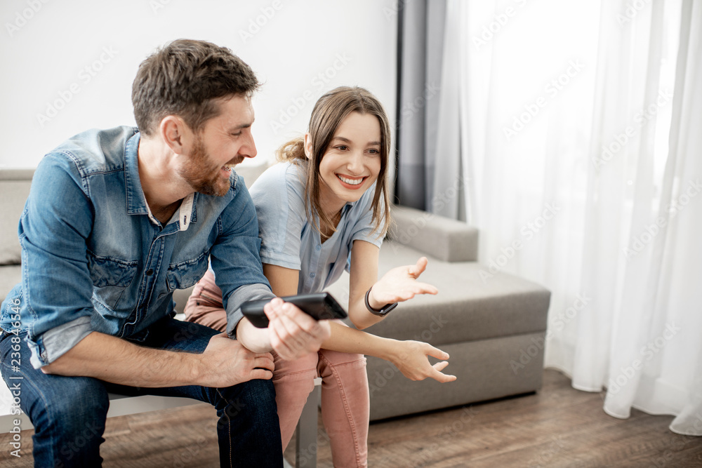 Young lovely couple with happy emotions watching TV sitting together on the table at home