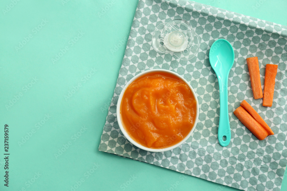 Bowl with healthy baby food on color table