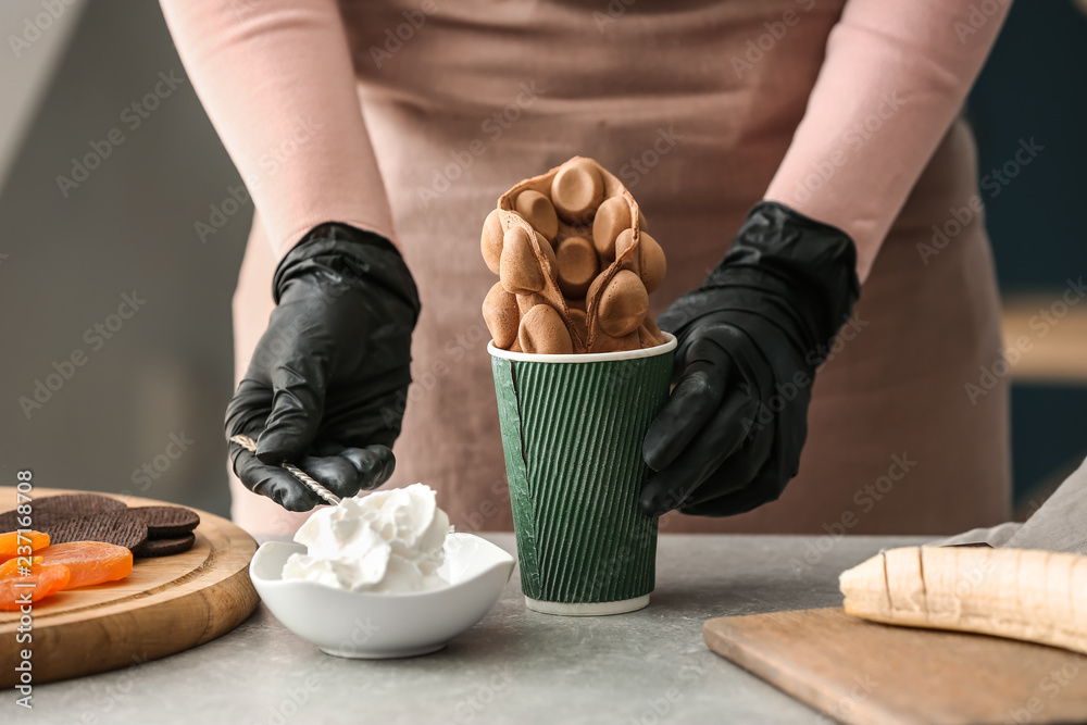 Woman preparing delicious bubble waffle with ice cream at table, closeup