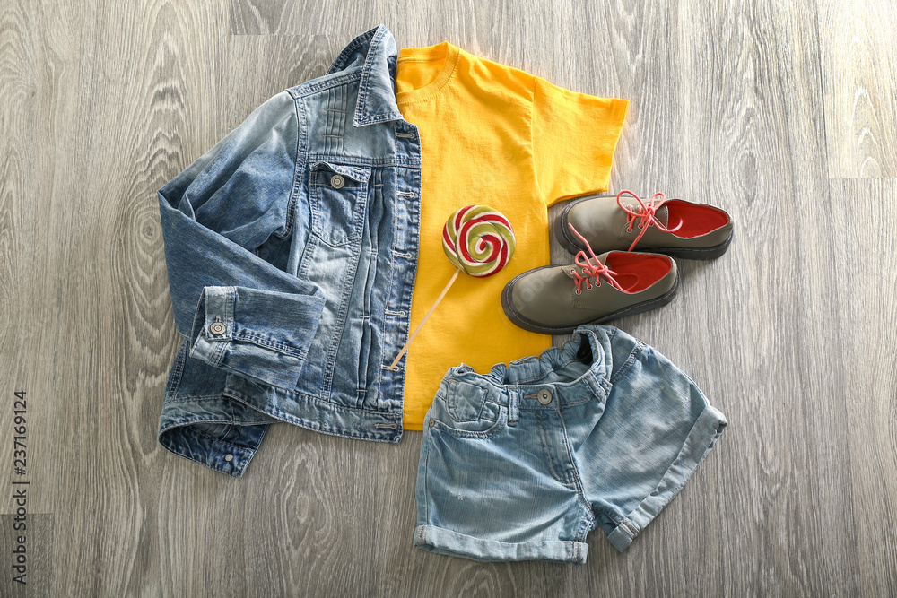 Stylish outfit with shoes and lollipop on wooden background