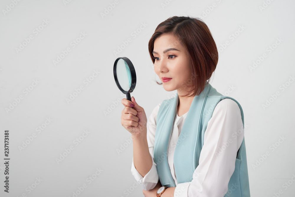 Close-up portrait of cheerful  woman in blue suite looking at camera through magnifying glass, isola