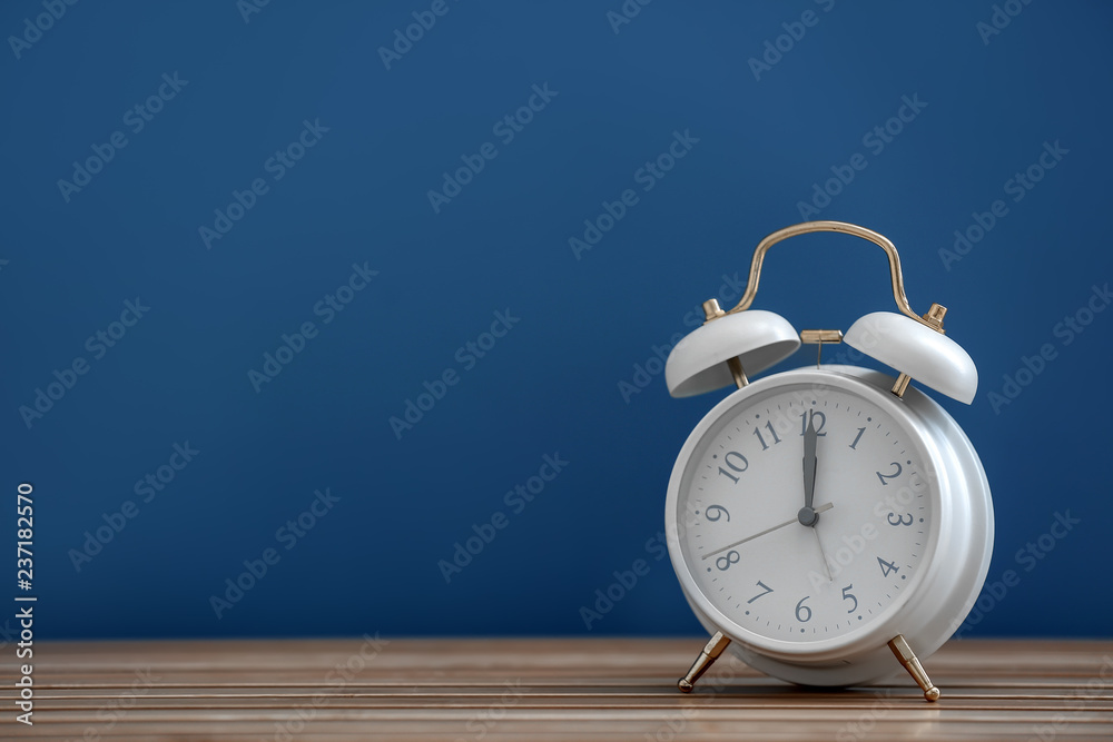 Alarm clock on wooden table against color background