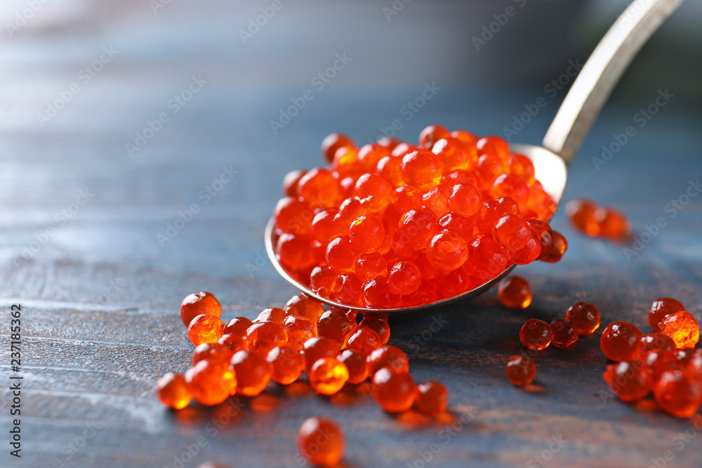 Spoon with delicious red caviar on color wooden table