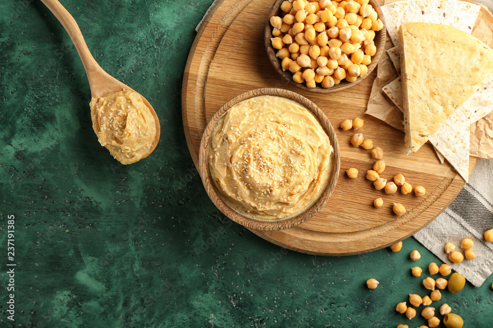 Bowls and spoon with hummus on color table