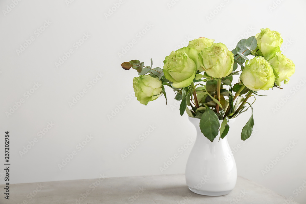 Vase with beautiful bouquet of green roses on table against light background