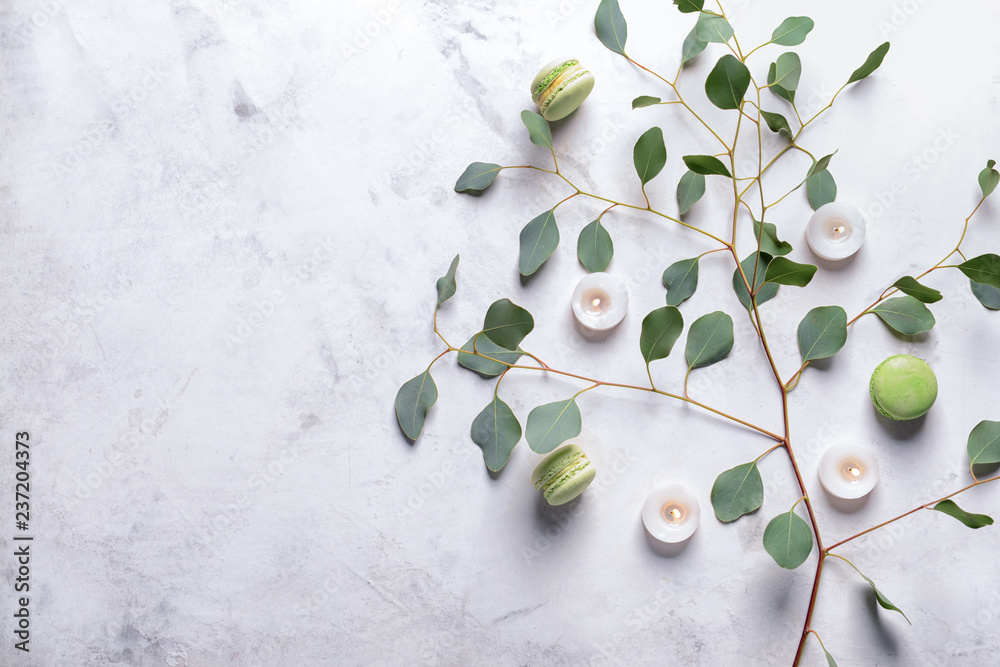 Burning candles with eucalyptus branch and macaroons on grey background