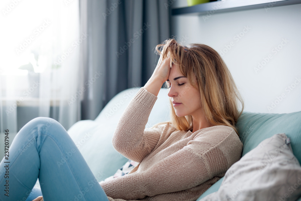 Depressed woman sitting on sofa at home, thinking about important things