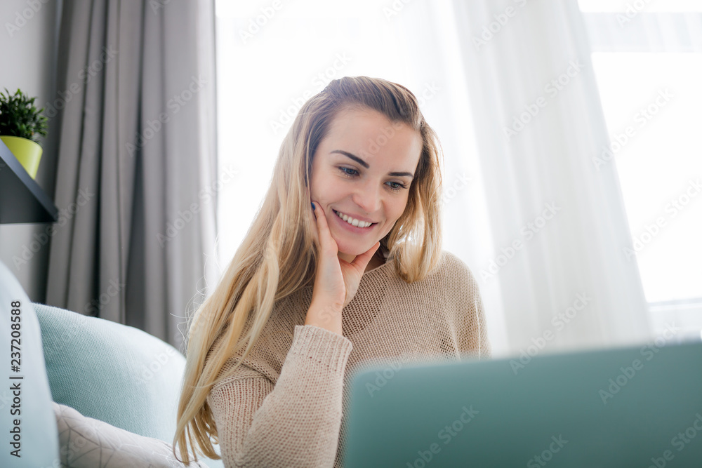 Happy woman at home using laptop sitting on sofa, online working at home