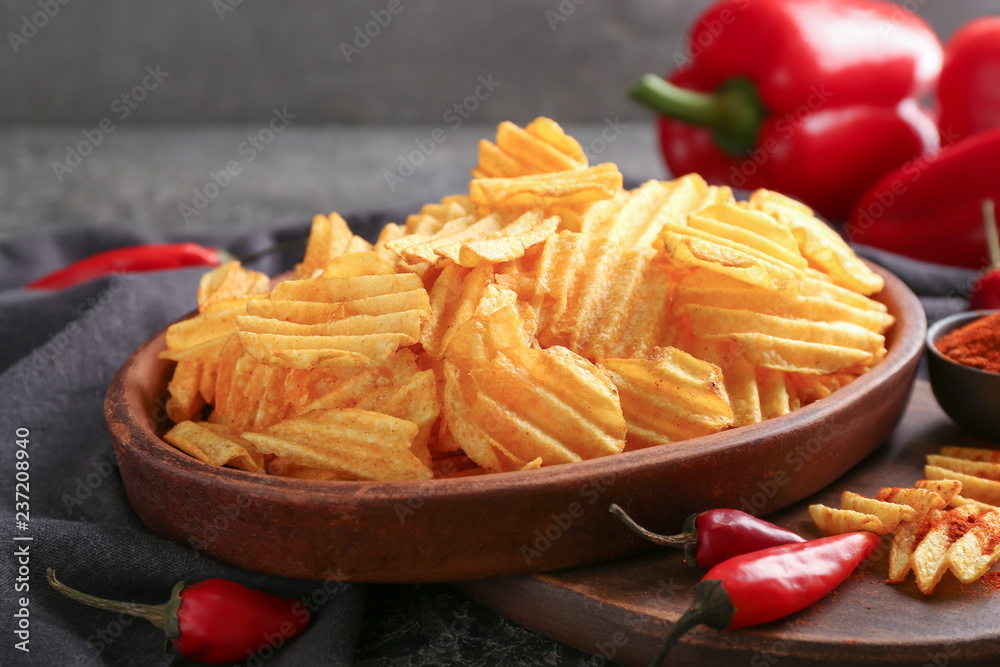 Bowl with tasty crispy potato chips on wooden board