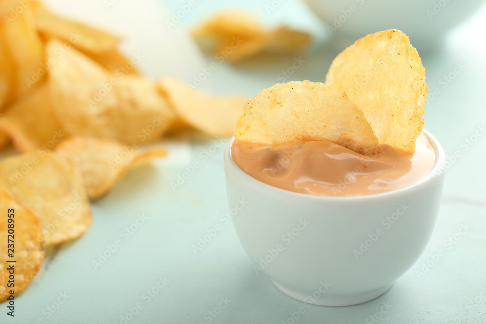 Tasty crispy potato chips in bowl with sauce on light table