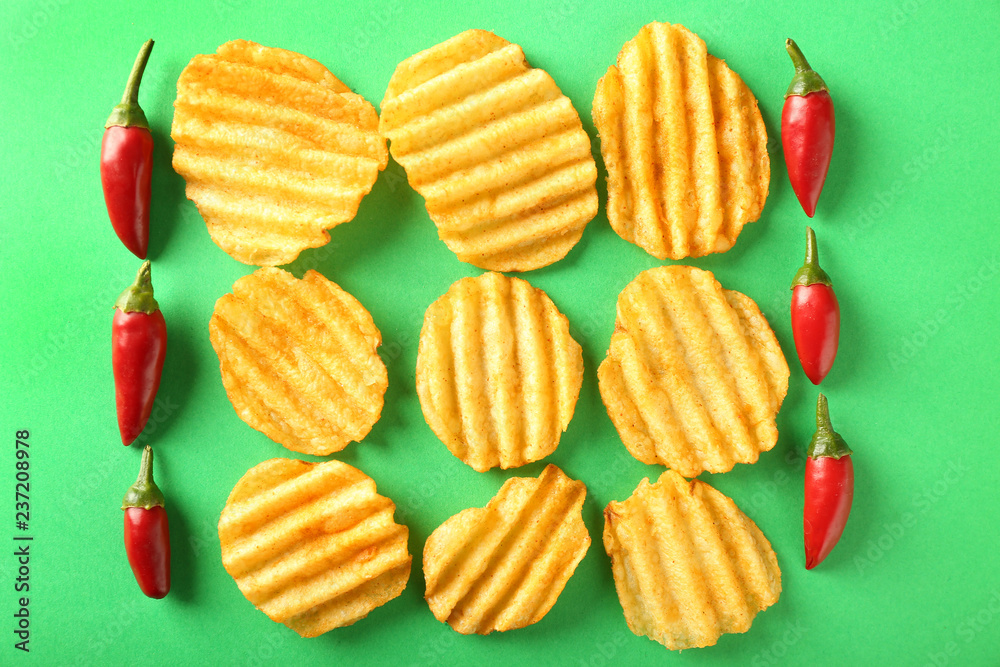 Tasty crispy potato chips with chili peppers on color background, top view