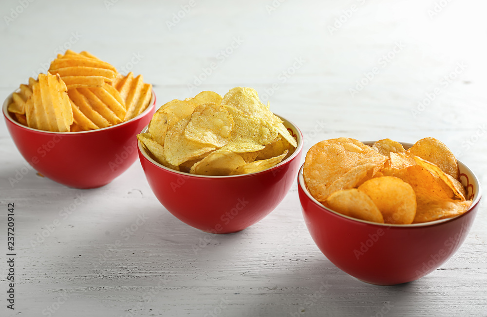 Bowls with tasty crispy potato chips on white wooden table