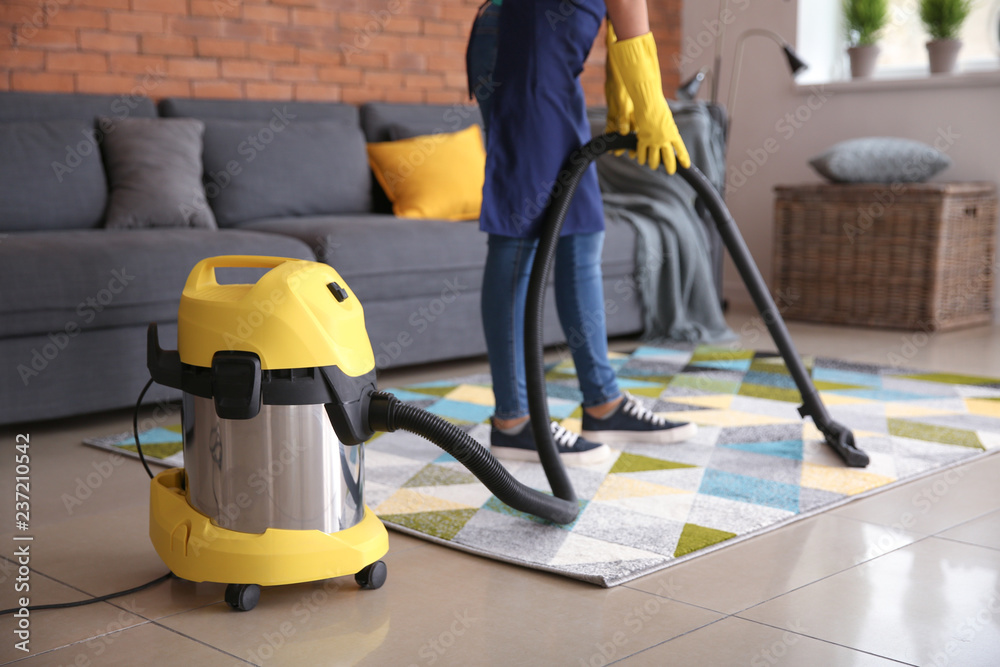 Female janitor hoovering carpet in flat