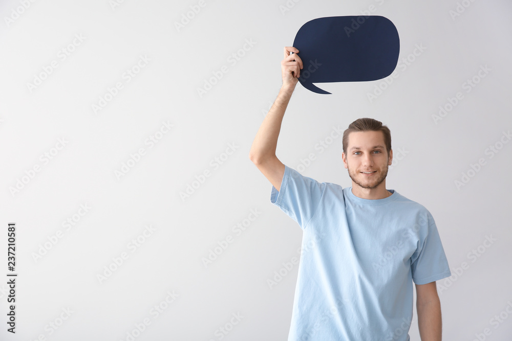 Young man with blank speech bubble on light background