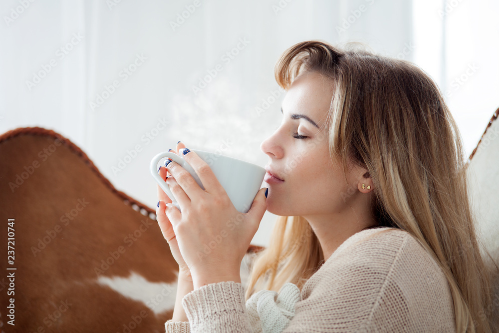 Happy woman sitting on armchair relaxing at home with cup of hot tea or coffee, positive emotions