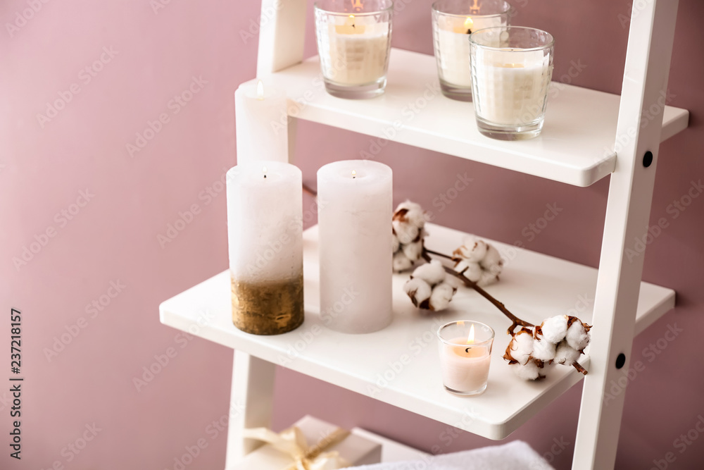 Many burning candles on shelves near color wall