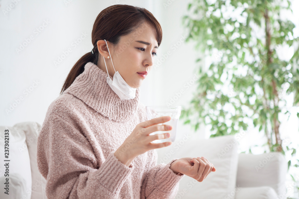 風邪を引き辛そうな女性が薬を飲んでいる