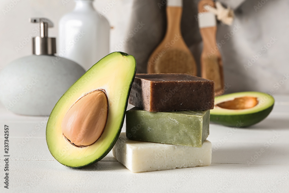 Soap bars with cut avocado on white table