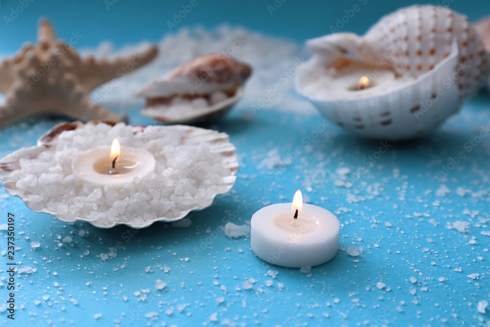 Burning candles with seashells and sea salt on color table