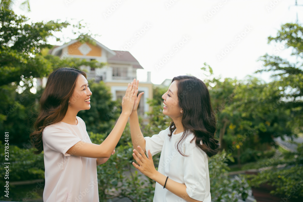 两个漂亮的年轻女人击掌-漂亮的女孩站在户外玩得很开心-最佳