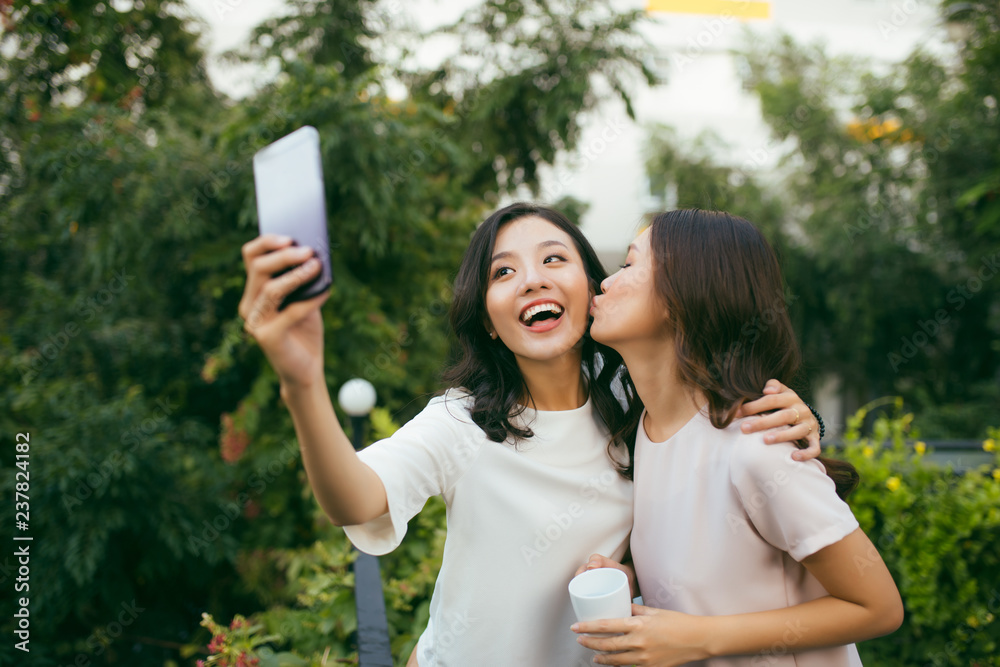 Lifestyle of Two beautiful Happiness Long Hair Women are  Using Mobile Phone for Selfie in Garden. A