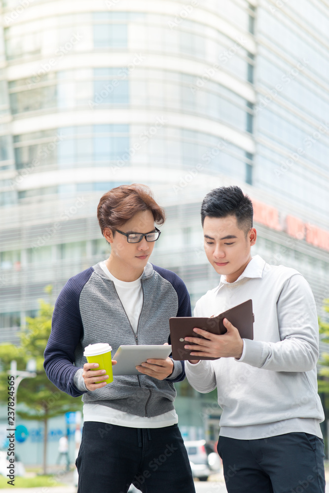 两位面带微笑的男性同事在户外通过数字平板电脑交谈