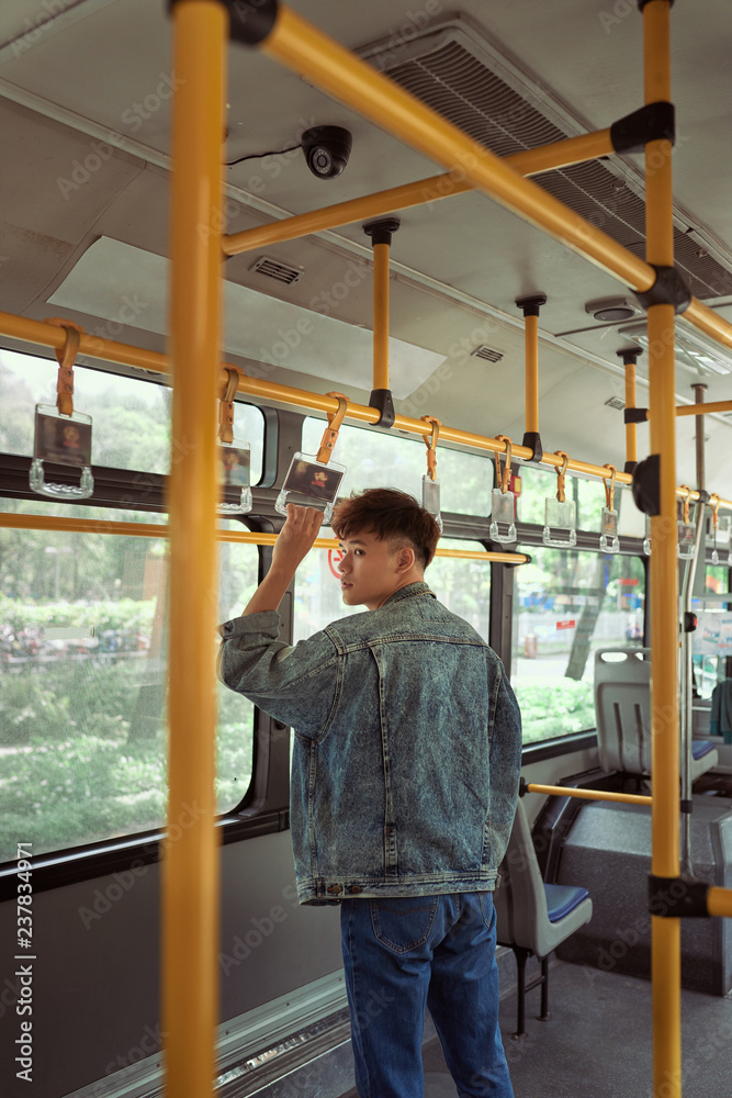 Young cheerful handsome man is holding onto the bar while standing in a bus.