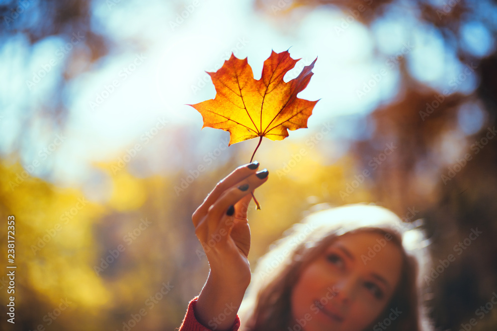 Natural woman holding colorful autumn leaf in bright sunlight