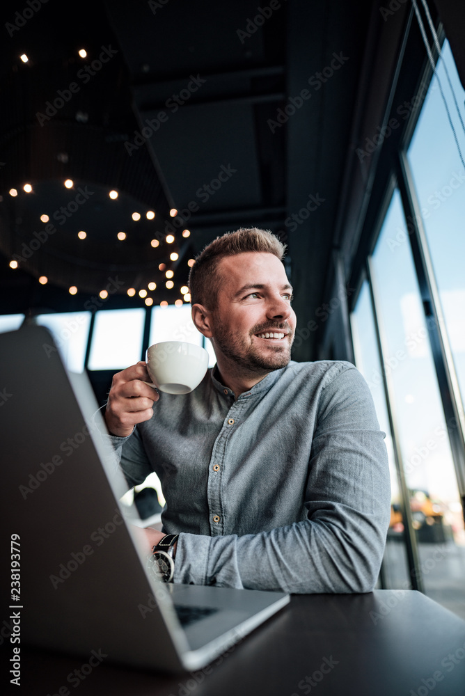 英俊的男人拿着笔记本电脑喝咖啡。低角度视角。