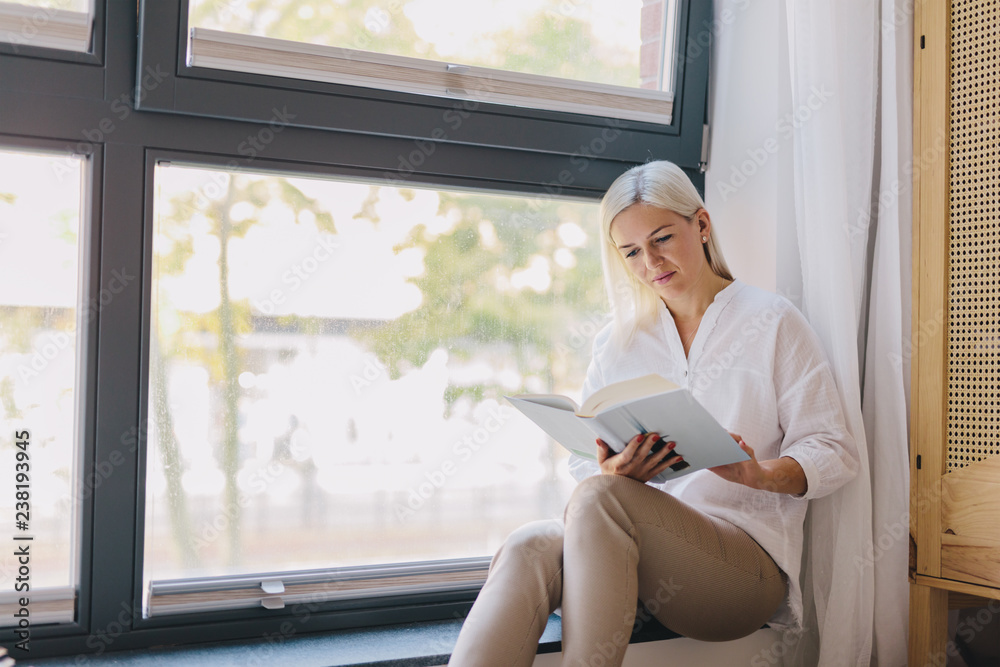 Woman reading book at home by the window.