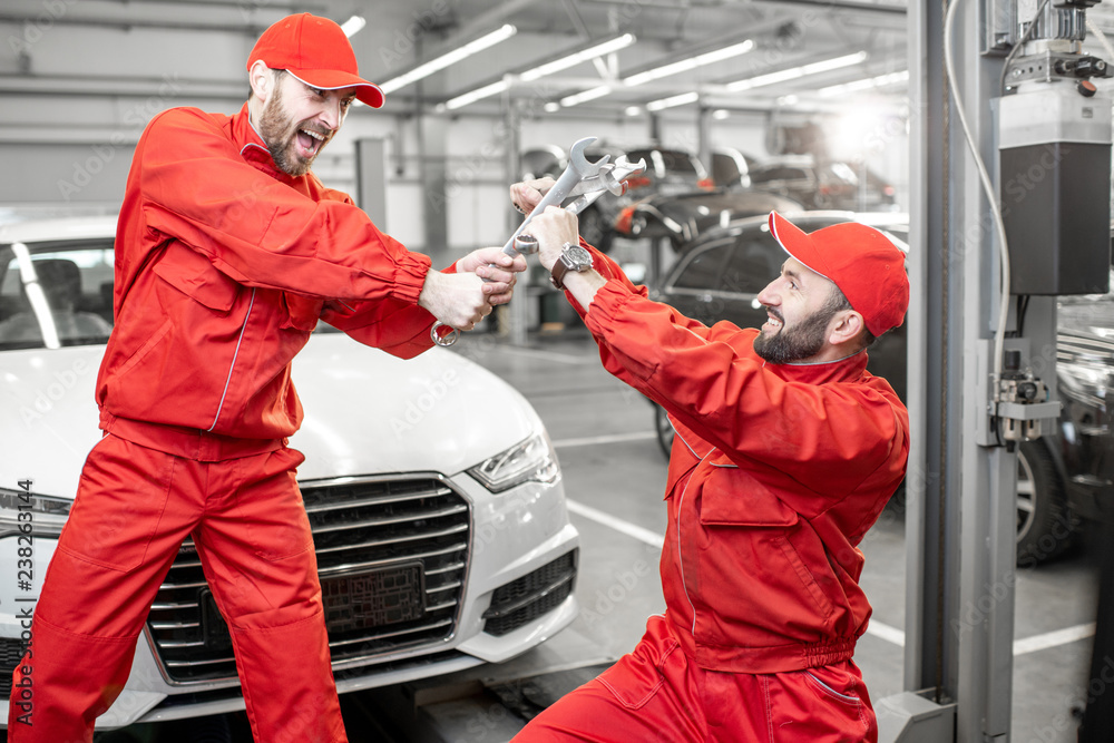 Funny portrait of two auto mechanics in red uniform fighting with wrenches in the car service