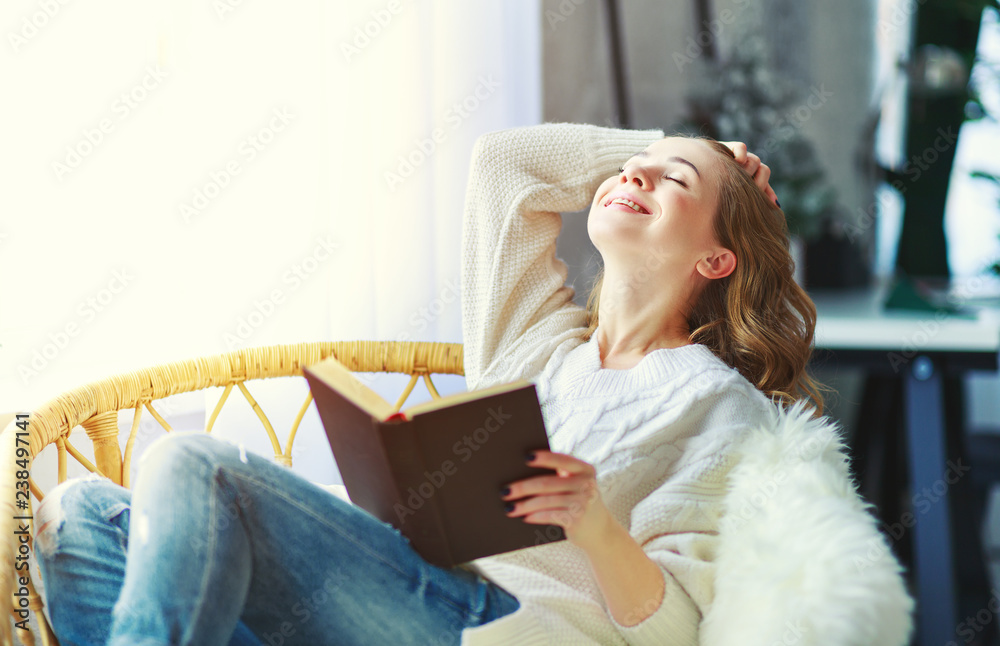 happy young woman reading a book by window