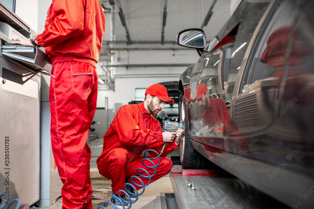 Two car service workers in red uniform changing wheel of a sport car at the tire mounting service