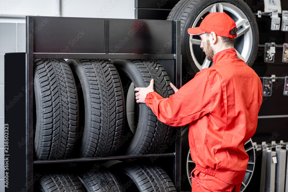 Car service worker in red uniform taking new wheel from the shelves of the wheel store