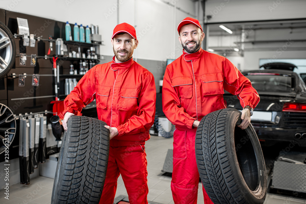 Portrait of a two car service workers in red uniform standing together with new tires at the store