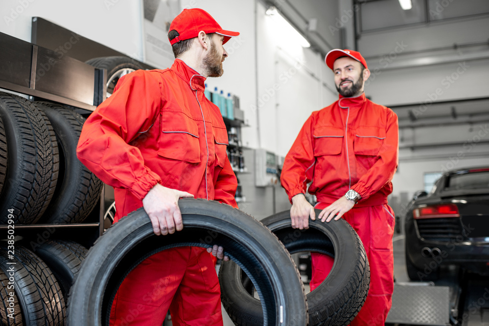 Car service workers in red uniform carrying new tires at the tire mounting service or shop