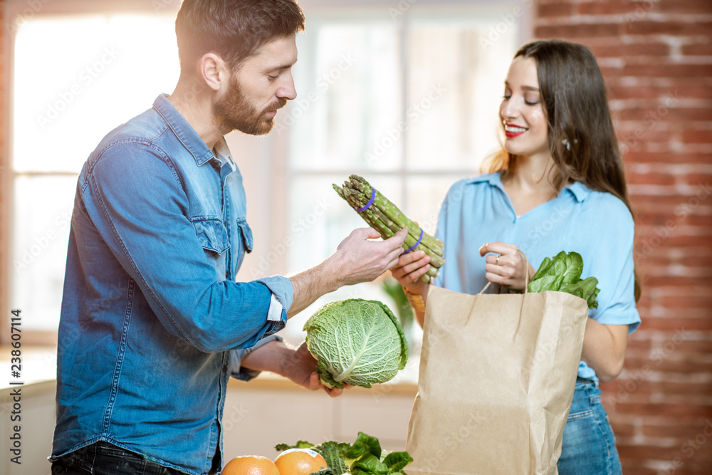 Young couple of vegetarians unpacking shopping back with fresh green product on the kitchen at home