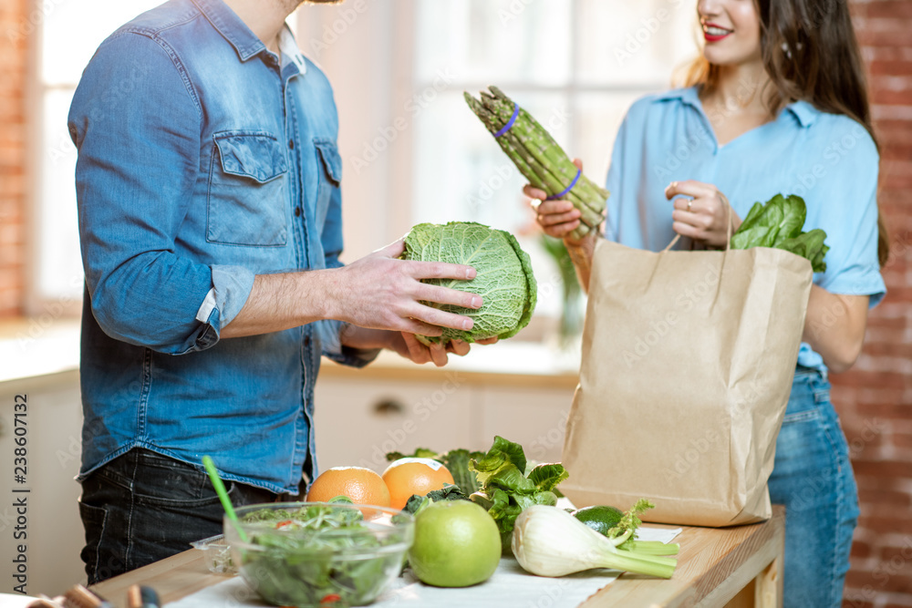 Young couple unpacking shopping back with fresh green products preparing to cook vegan meals on the 