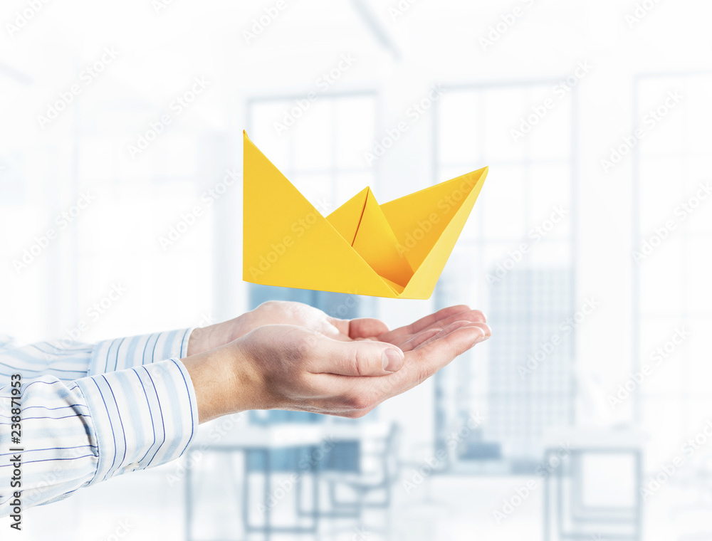 Origami boat in male palms against modern interior background. M