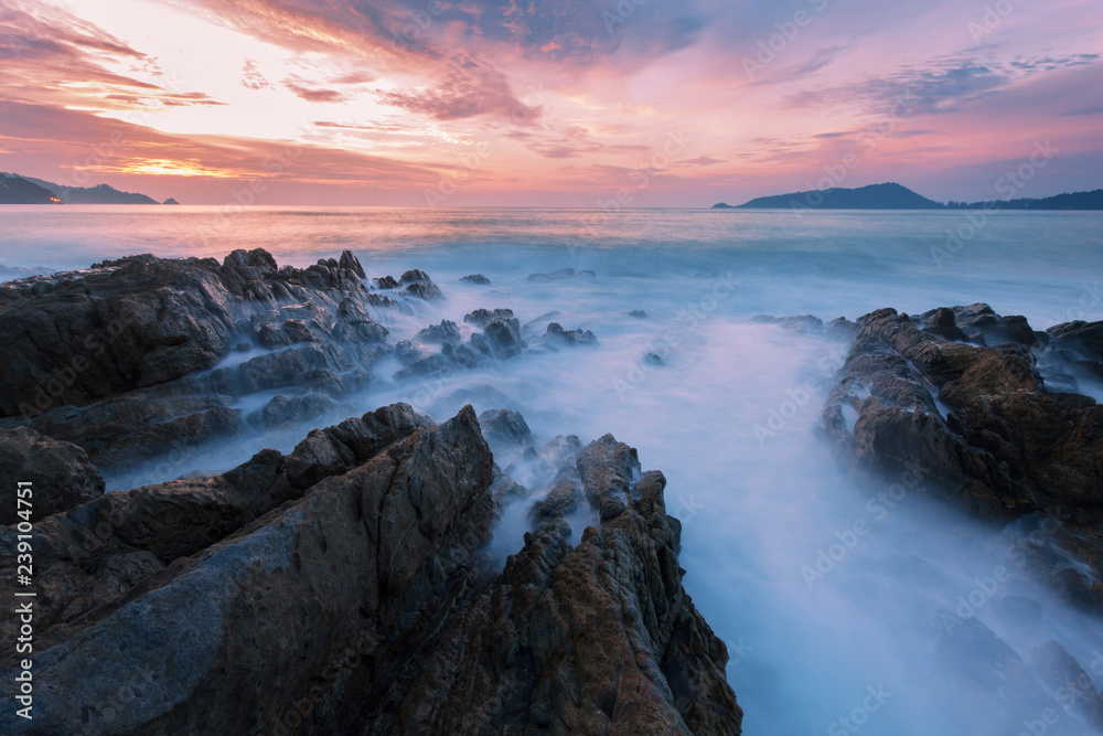 Long exposure image of Dramatic sky and wave seascape with rock in sunset scenery background.