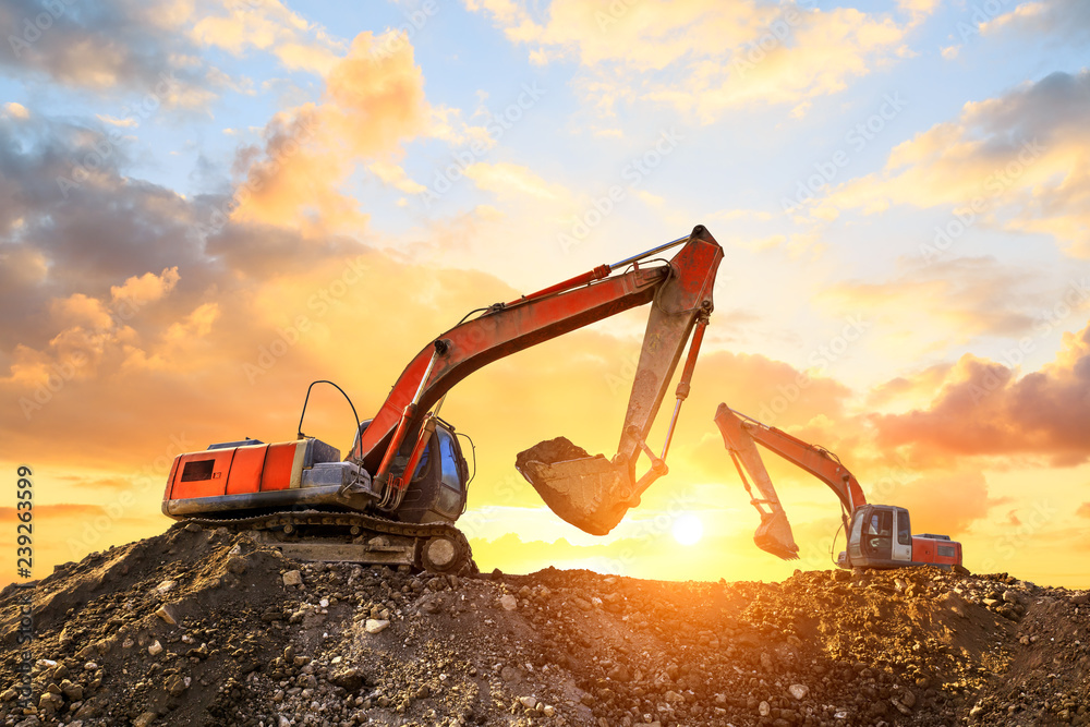 Two excavators work on construction site at sunset